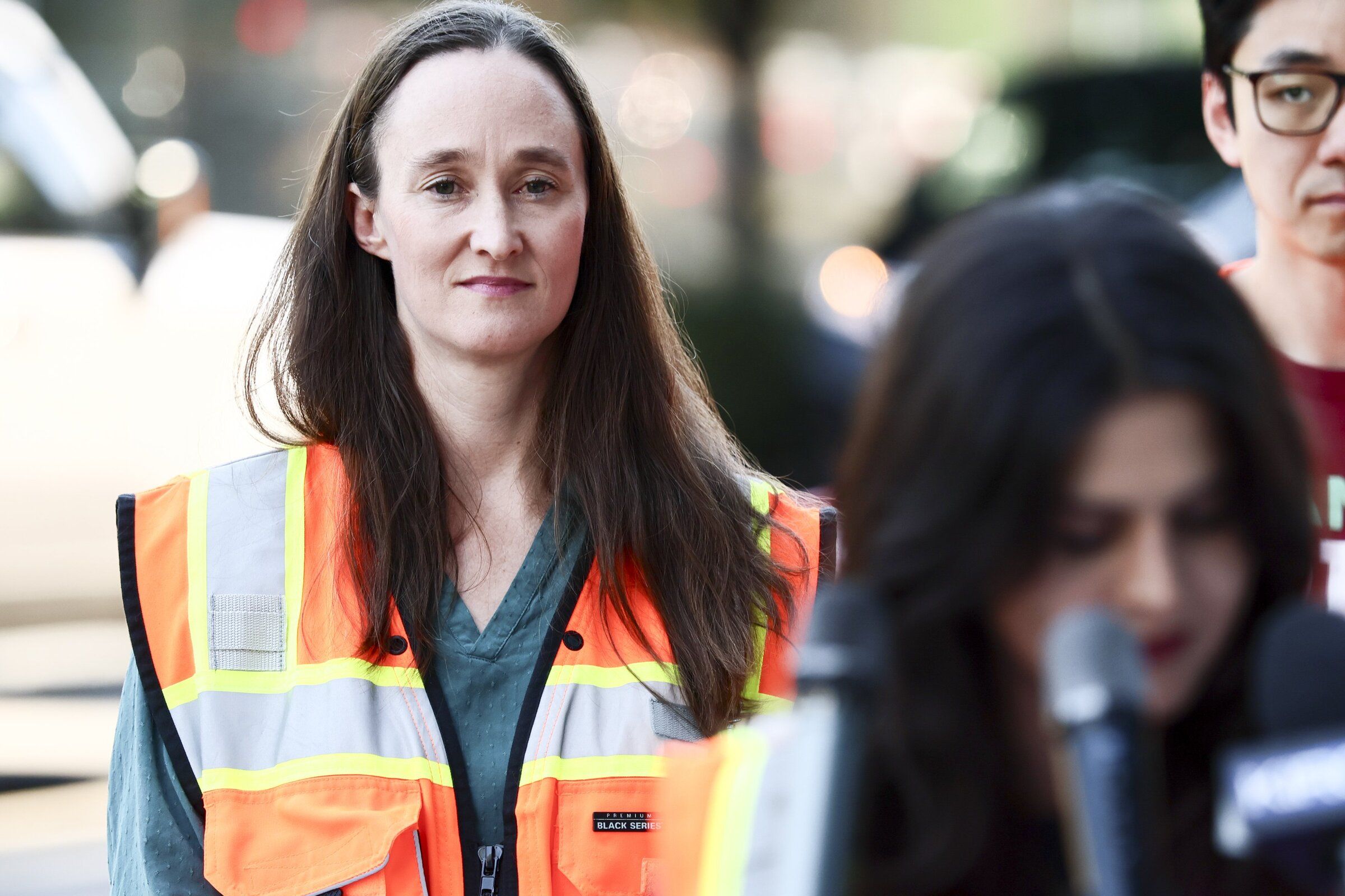 Seattle Mayor Katie Wilson, as City Councilmember Alexis Mercedes Rinck addresses the news media on Denny Way. (Kevin Clark / The Seattle Times)