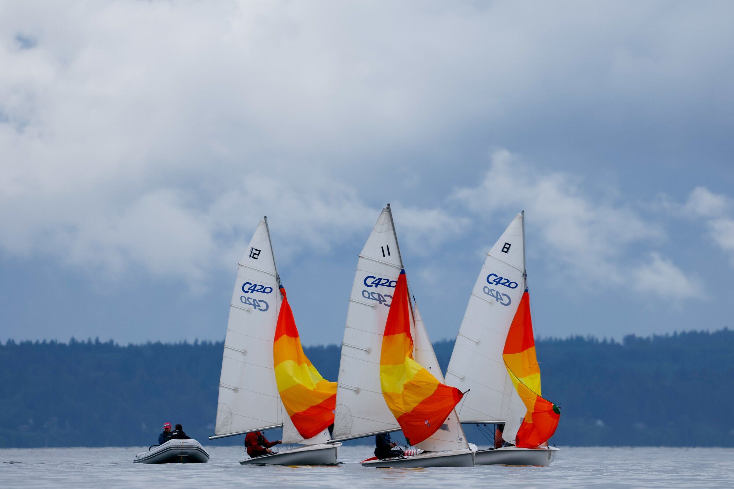 Dramatic storm clouds obscure the Olympic Mountains as small sailboats unfurl colorful spinnakers as they practice maneuvers near Shilshole Saturday, June 6, 2026 in Seattle. (Jennifer Buchanan / The Seattle Times)