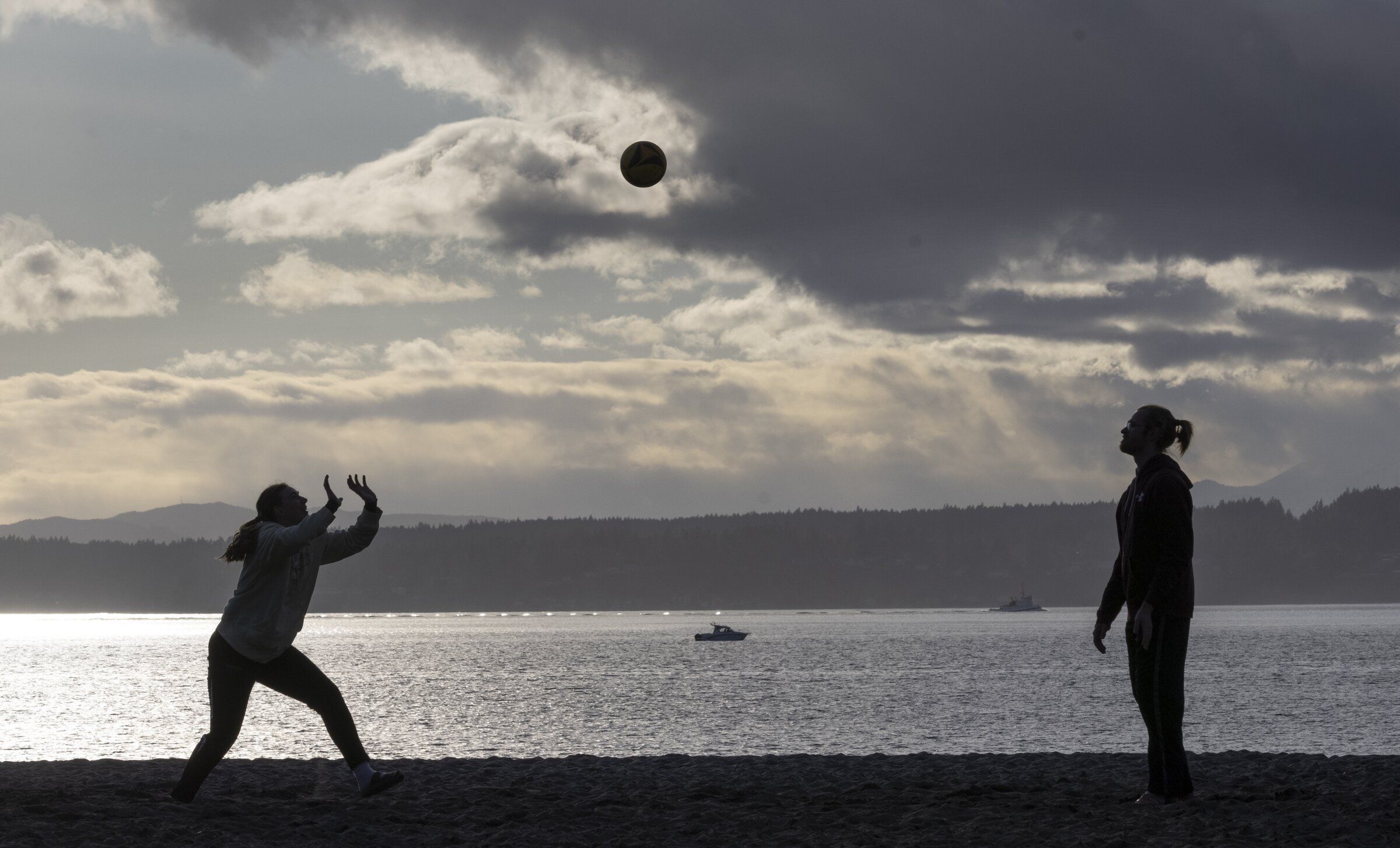 Marybeth Ohanlon, left, and Austin Bryan play volleyball under a mix of sun and clouds at Golden Gardens Park earlier this year. (Ellen M. Banner / The Seattle Times)