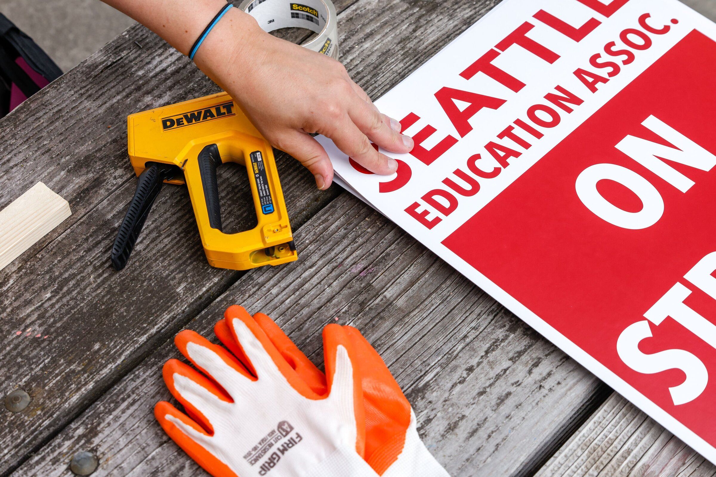 Alessia Fitz Gibbon, whose partner teaches at Garfield High School, grabs a sign to staple onto a wooden stick as educators with the Seattle Education Association make signs at Judkins Park in Seattle on Saturday, Aug. 29, 2026, following a strike authorization. (Andrew Burke-Stevenson / The Seattle Times)
