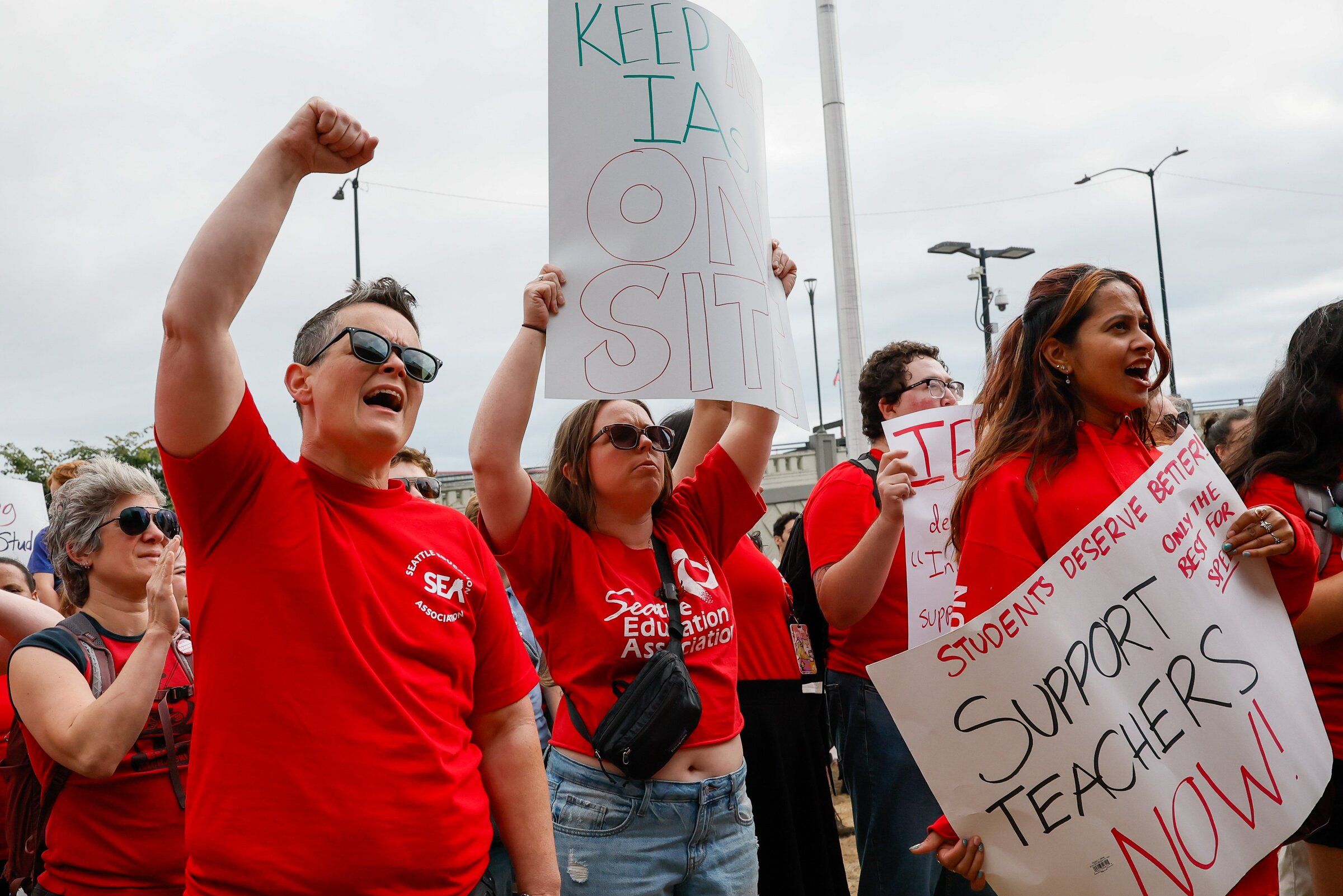 From left, Dylan Bosseau, a preschool teacher at B.F. Day Elementary, joins with Karly Muller at center, a teacher at Salmon Bay K-8, and Roshni Sinha, who was supporting her girlfriend Natalie Reeder, also a teacher at Salmon Bay K-8 during a Seattle Education Association rally outside the Seattle Public Schools headquarters Tuesday, Sept. 1, 2026 in Seattle. (Jennifer Buchanan / The Seattle Times)