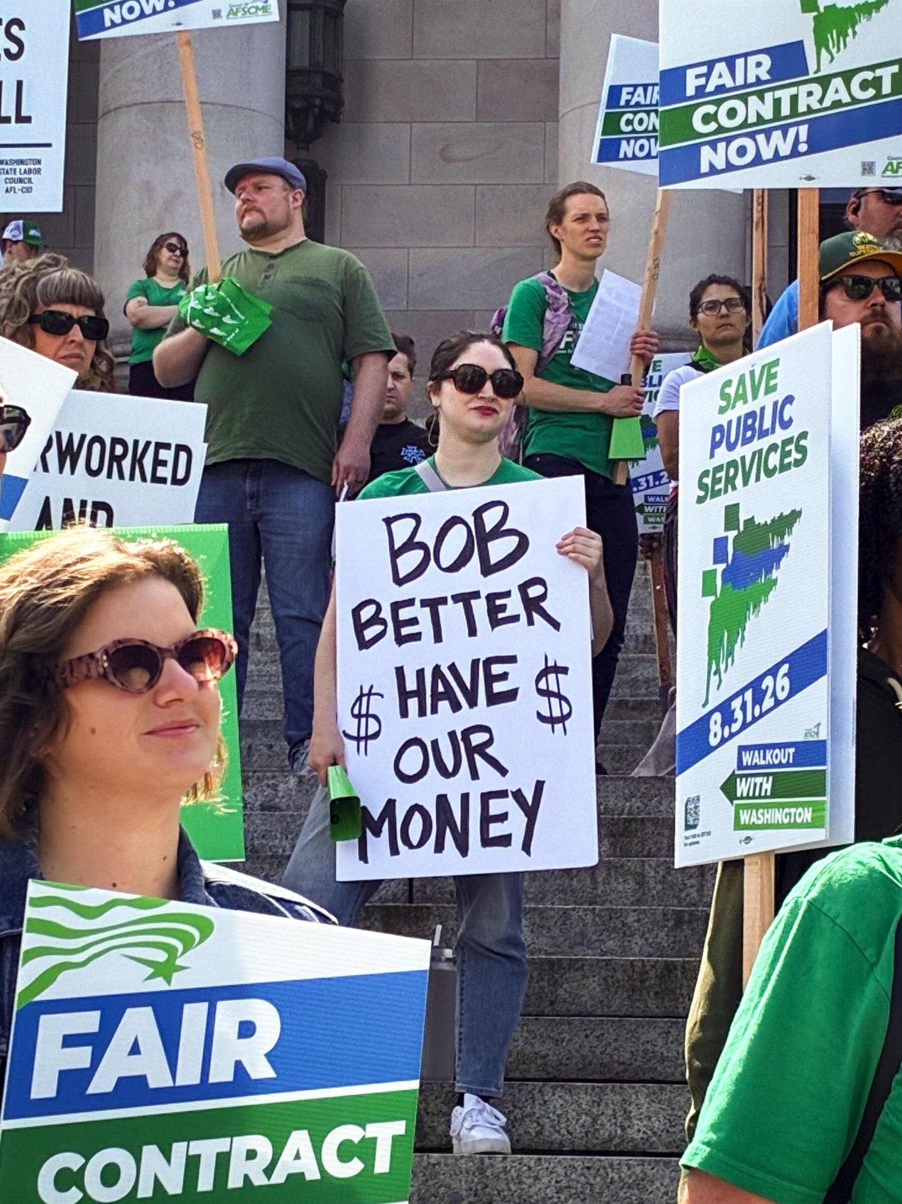 Zoë Ortega, 25, holds a sign calling on Gov. Bob Ferguson to approve a collective bargaining agreement with raises for state employees during a rally in Olympia on Saturday. (Joseph O’Sullivan / The Seattle Times)