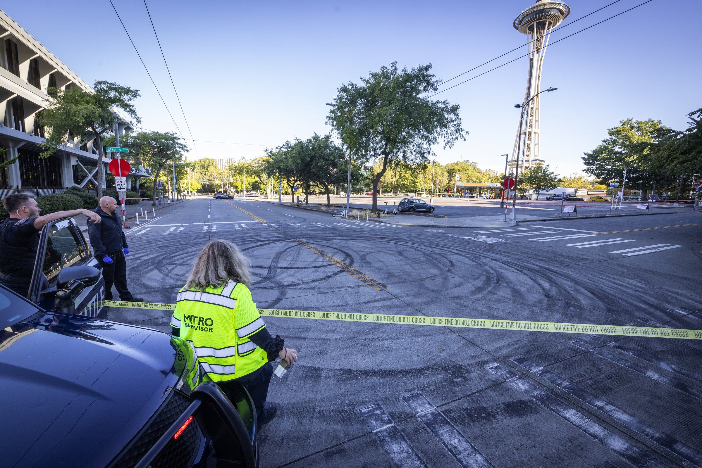 A Metro inspector stands to the right of Seattle police officers after bus service was suspended while they examine the scene where cars were drifting and spinning their tires at the intersection of Clay Street and Third Avenue; a crime scene linked to a fatal shooting is being investigated in Belltown on Sunday. It was one of two fatal shootings in Belltown overnight. (Ken Lambert / The Seattle Times)
