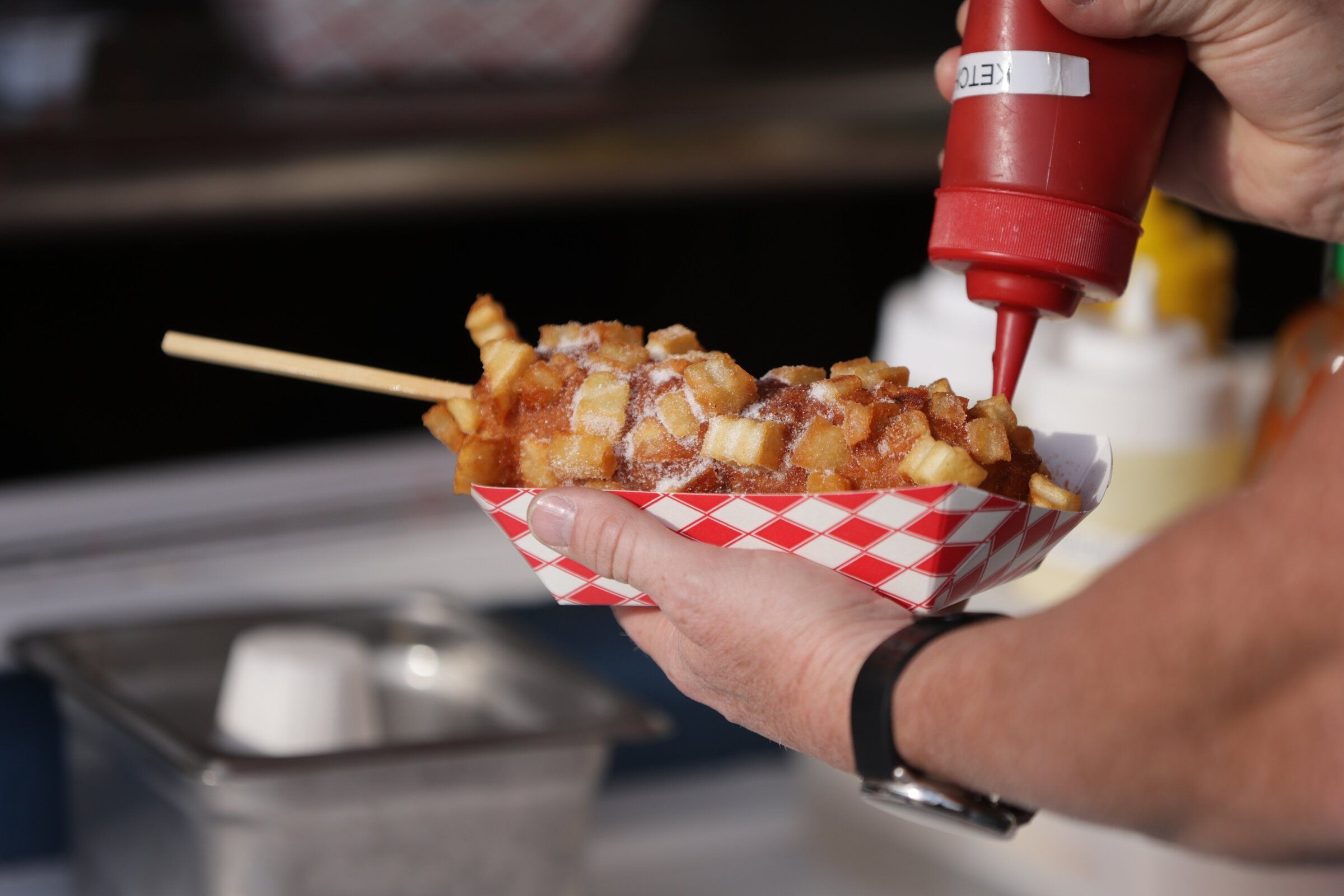 A visitor adds ketchup to a potato-topped hot dog at Seoul Hotdog at Wild Waves on Aug. 29. (Genna Martin / special to The Seattle Times)