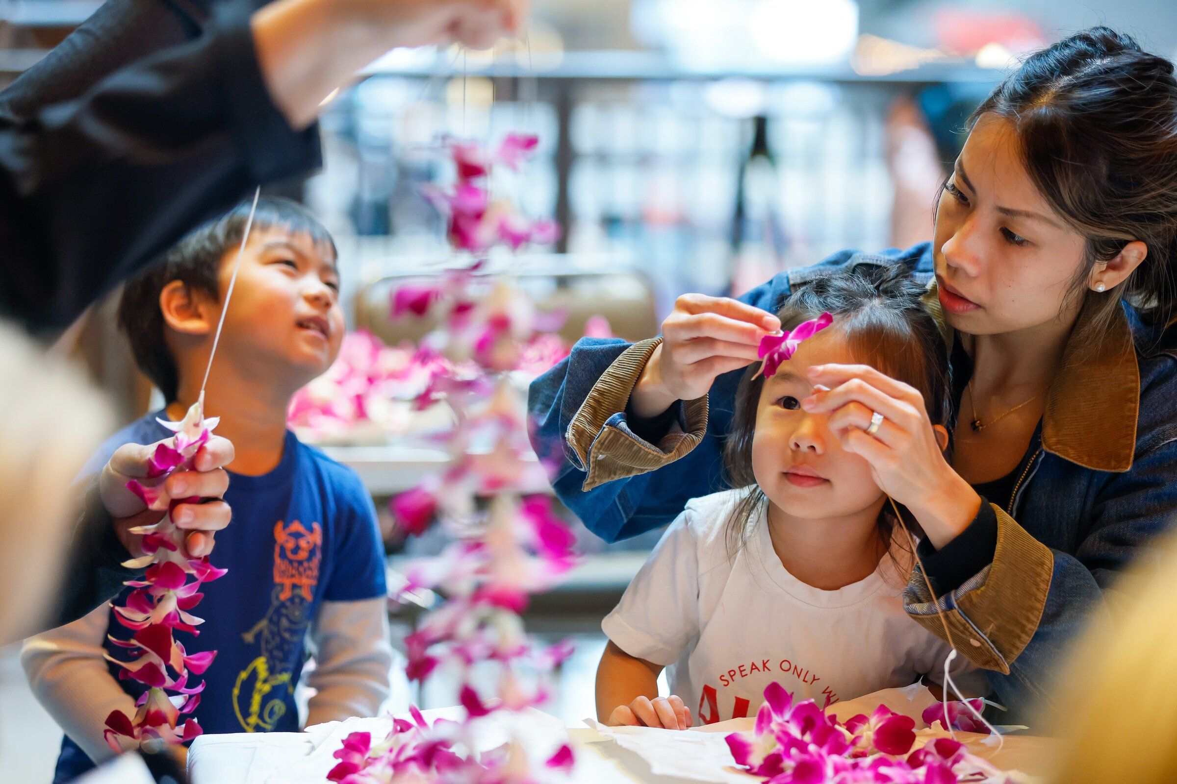 Harlow Van, 3, at right, looks up at the lei her mom Jessica is making while Harlow’s best friend Sky Kao, also 3, helps his dad Mike assemble one during the Live Aloha Hawaiian Cultural Festival at the Seattle Center on Sunday in Seattle. (Jennifer Buchanan / The Seattle Times)