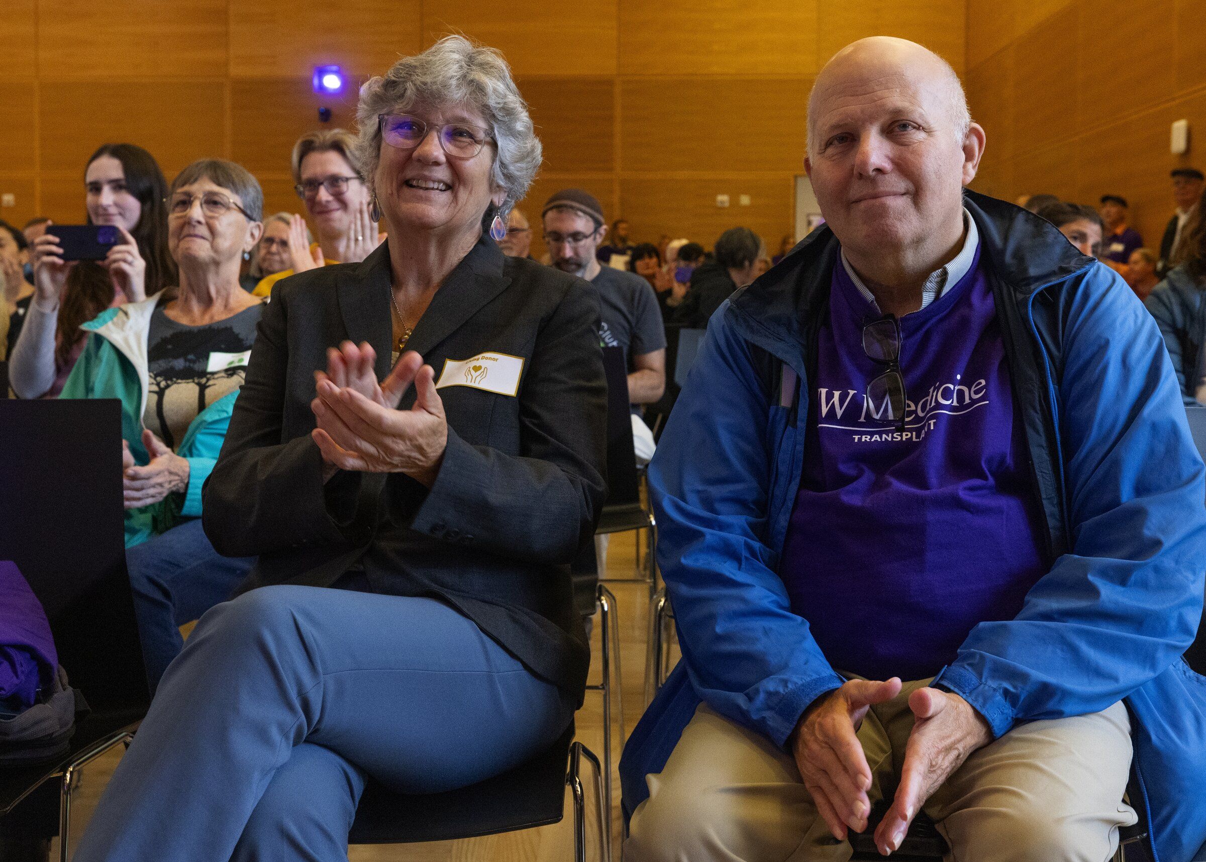 Diana Simms sits beside George Sharp, who received a kidney from Simms in 2024, during a “transplant recipient picnic” Sunday on the University of Washington campus in Seattle. They listen to speakers after Simms herself spoke. (Ken Lambert / The Seattle Times)