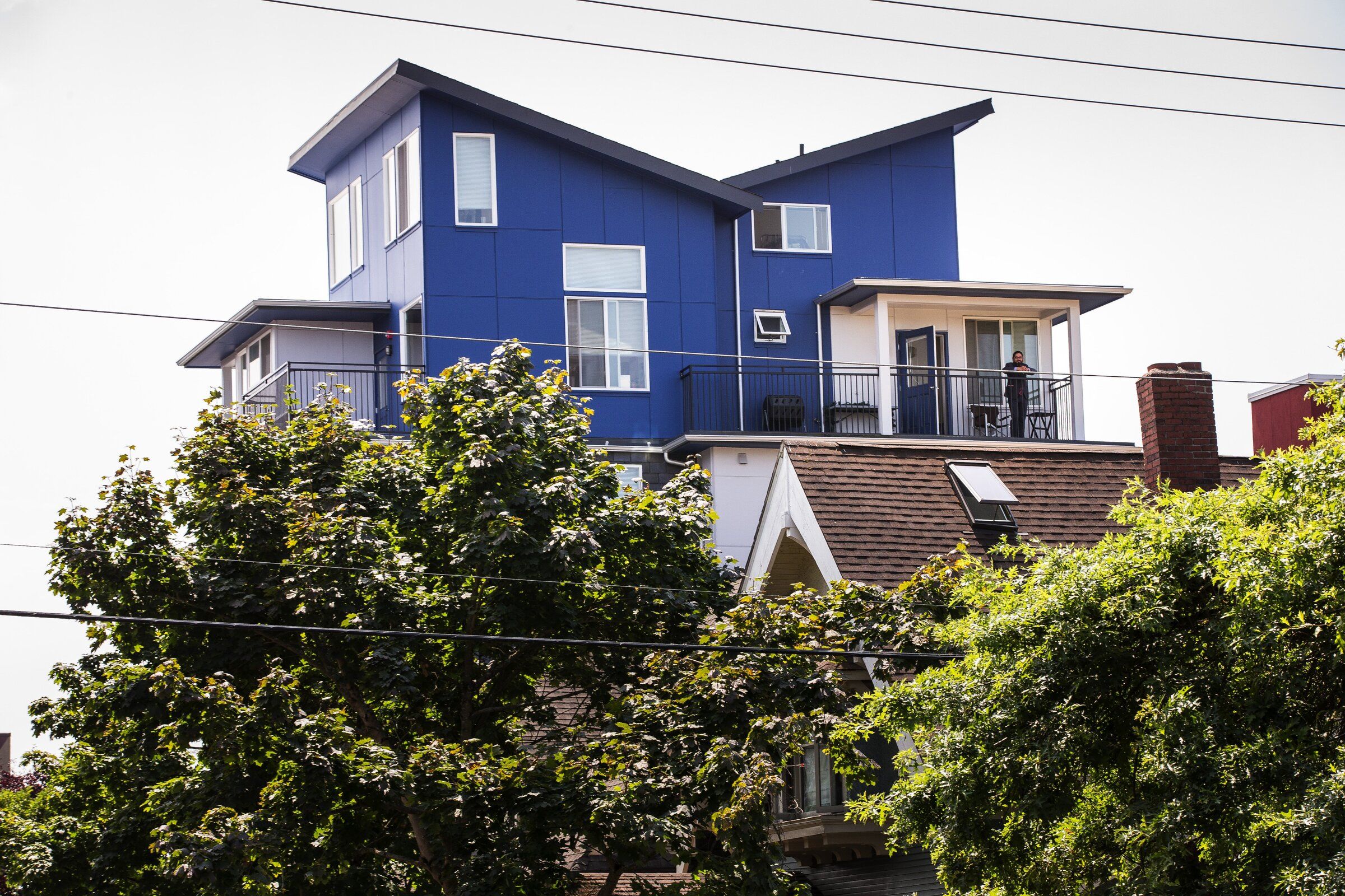 Roger Valdez is seen in the upper right, standing on the balcony of his apartment in the Apodment building, which overlooks Lake Union to the north and the Space Needle to the west. (Dean Rutz / The Seattle Times, 2015)