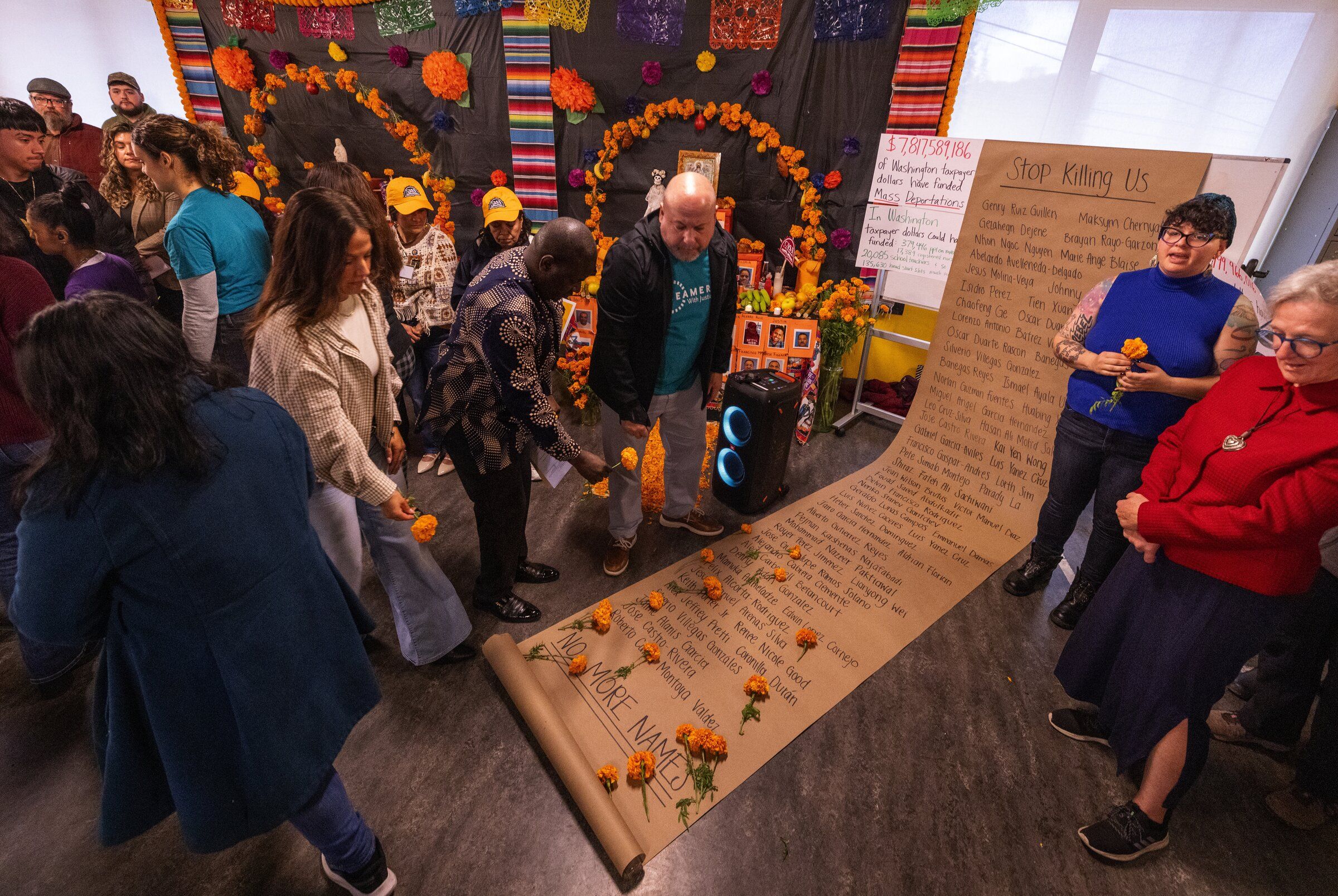 At a news conference at Casa Latina in Seattle on Tuesday, people place marigolds atop a list of people immigrant advocates said have died in detention or during ICE arrests nationwide. More than a half dozen organizations gathered to draw attention to the impact of ceaseless detentions and to call on elected officials and ordinary residents to get involved. (Ken Lambert / The Seattle Times)